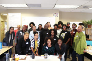 A group of Black people in a room with desks stand together, smiling