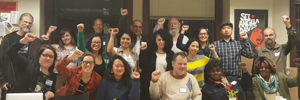 Picture of the Displaced Tenants a group of white asian Black and brown people gathered together at an office with smiling with their fists raised