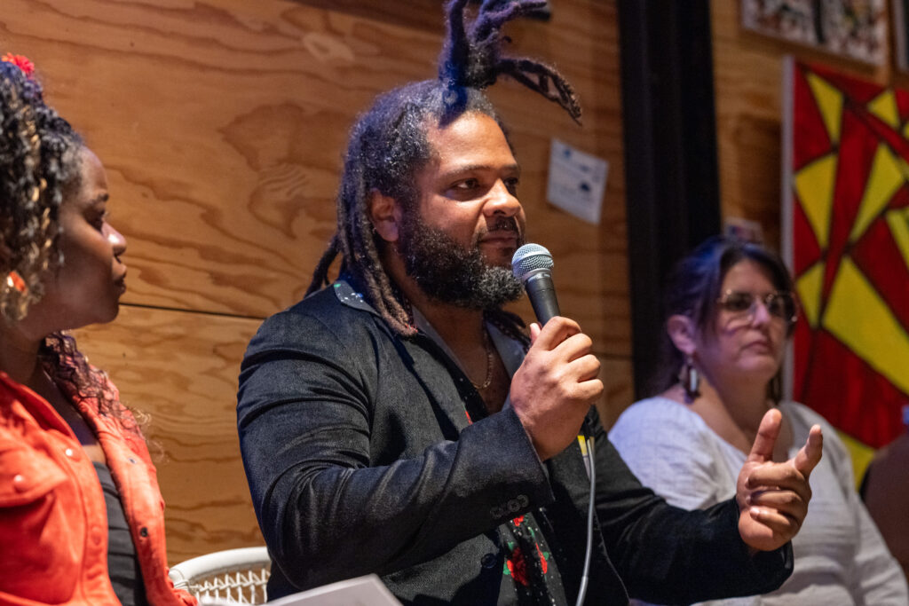 A photo of JT holding a microphone and speaking passionately at SJF's Rise Seattle event. 